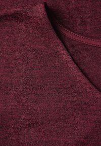 Burgundy strikstof med en glat tekstur, der har en V-hals design og en subtil meleret mønster. Let ribbet kravedetalje.