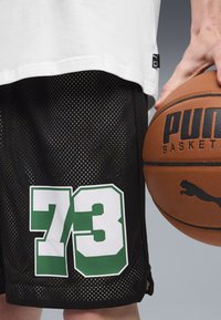 Pantalones cortos de baloncesto de malla negros con el número 73 en verde y blanco en la pierna, usados con una camiseta blanca y sosteniendo un balón de baloncesto marrón.