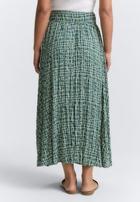 Jupe maxi à motif vert présentant un design en quadrillage crème, fabriquée en tissu léger, avec une taille élastique et des détails plissés.