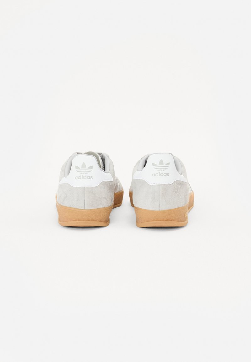 Zapatillas de ante grises con suela de goma y etiqueta en el talón blanca que presenta el logo de Adidas; forma redondeada con tejido texturizado.