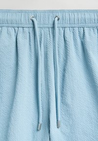 Shorts de culoare albastru deschis, cu o textură, având un brâu elastic. Prezintă două sfori cu capete metalice argintii. Materialul are un aspect creponat.