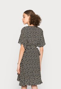 Vestido preto com padrão floral em creme e castanho claro, mangas esvoaçantes, cintura amarrada e bainha com babados, feito de um tecido leve.