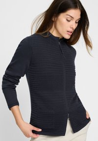 Donker marineblauwe gebreide cardigan met ritssluiting, geribbelde manchetten en twee getextureerde zakken; voorzien van een gestreept patroon voor extra detail.