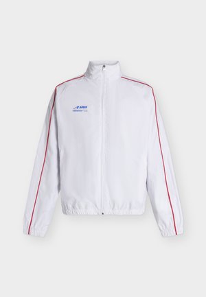 Veste sportive blanche zippée avec un liseré rouge le long des manches, des poignets et un ourlet élastiques, et un logo "ARKK" bleu sur la poitrine.