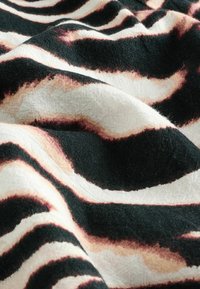 Tekstil s uzorkom crno-bež zebra pruga, s mekom, teksturiranom površinom i fluidnim drapiranjem, koje prikazuje kontrastne boje.