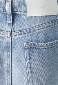 Svetlomodré džínsy z denimu s vreckom na zadnej strane, výrazným prešívaním a bielou koženou značkovou etikou na páse.