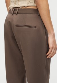 Καφέ παντελόνια προσαρμοσμένης ραφής χαρακτηρίζονται από μια ομαλή υφή, επίπεδη μέση και τσέπη με welt στην πλάτη, με καθαρό, δομημένο σχεδιασμό.