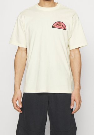 T-shirt à manches courtes couleur crème avec un col rond. Présente un graphisme "Basketball Nike Hoops" en rose et noir sur la poitrine.