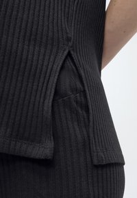 Κοντινή λήψη μαύρου μπλουζιού με ριμπ ύφασμα και πλαϊνή σχισμή πάνω από αντίστοιχο παντελόνι με ριμπ ύφασμα, που δείχνει την υφή και τα στρώματα ρούχων.