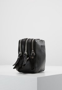 Borsa in pelle nera con tre scomparti con zip, finitura testurizzata distintiva, accessori in argento e tirazip piatti. Forma rettangolare compatta.