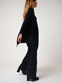 Poncho en tricot bleu marine avec un col haut et une coupe ample, associé à un jean en denim large et sombre et des bottines à talons chunky.