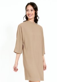 Rochie bej până la genunchi, realizată dintr-un material neted, cu un decolteu înalt și mâneci scurte, largi. Design simplu, minimalist, fără modele.
