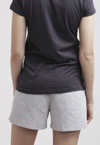 Personne portant une chemise à manches courtes gris foncé et un short rayé gris clair et blanc, debout de dos face au spectateur.