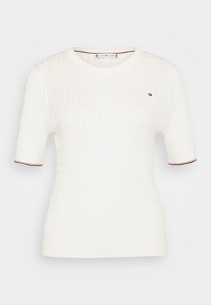 Hvid kortærmet strikket top med et tekstureret mønster, der har en rund halsudskæring og røde samt blå accenter ved ærmeenden.