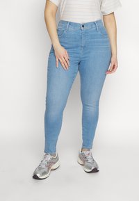 Lysblå skinny jeans med høj talje, femlomme-design og lynlås; parret med grå sportssko og en stribet skjorte.