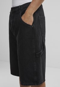 Pantalones cortos de mezclilla negros con un ajuste relajado, que cuentan con bolsillos laterales, costuras visibles y una textura suave. Diseñados para un uso casual.