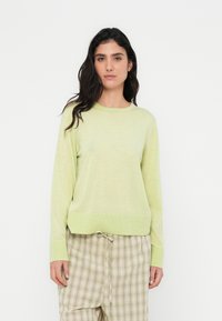 Ανοιχτοπράσινο πουλόβερ με μακριά μανίκια, στρογγυλή λαιμόκοψη, ριμπ μανσέτες και ελαφρώς φαρδιά εφαρμογή, σε συνδυασμό με καρό καρό παντελόνια.