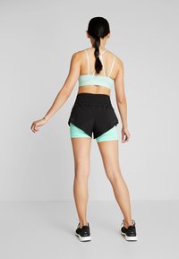 Sportbehå i ljus mintgrön, tillsammans med svarta shorts med ett lagerdesign. Outfitten kompletteras med svarta träningsskor.