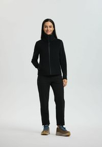 Sort fleecejakke med høj krave og lynlås, parret med sorte bukser og brune vandresko. Glat tekstur og strømlinet design.