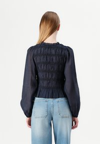 Navy smocked blouse with long, puffed sleeves and a gathered neckline, paired with light blue denim jeans. Smooth fabric texture.