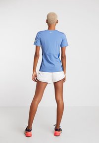 Ljusblå träningsskjorta med korta ärmar, med kontrasterande blå sidopaneler och en liten logo på baksidan, kombinerad med vita shorts.