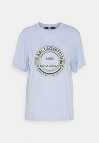Světle modré bavlněné tričko s oblíbeným kruhovým grafickým vzorem, které obsahuje text "Karl Lagerfeld", "Paříž" a "21 Rue St-Guillaume" v černé a zelené barvě.