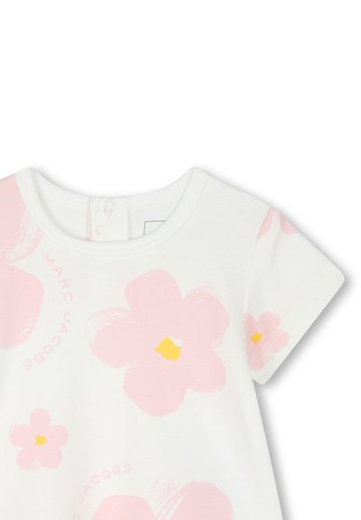 T-shirt bianco in cotone con maniche corte, caratterizzato da grandi stampe di fiori rosa con centro giallo. Include una scollatura rotonda e chiusura a snaps sul retro.