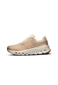 Beige athletic shoe with a textured upper, white cloud-like midsole, and gum rubber outsole. Features laces and logo detail on the side.
