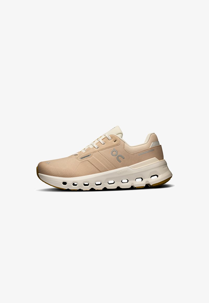 Beige athletic shoe with a textured upper, white cloud-like midsole, and gum rubber outsole. Features laces and logo detail on the side.