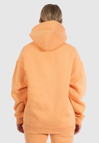 Overmaat hoodie in pasteloranje stof. Heeft een grote capuchon, ribgebreide manchetten en zoom. Soepele textuur met een casual, relaxte pasvorm.