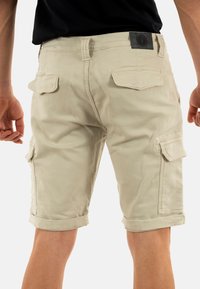 Pantaloni cargo beige di lunghezza ginocchio realizzati in cotone, dotati di molteplici tasche, orli arrotolati e una cintura testurizzata con un'inserzione del logo.