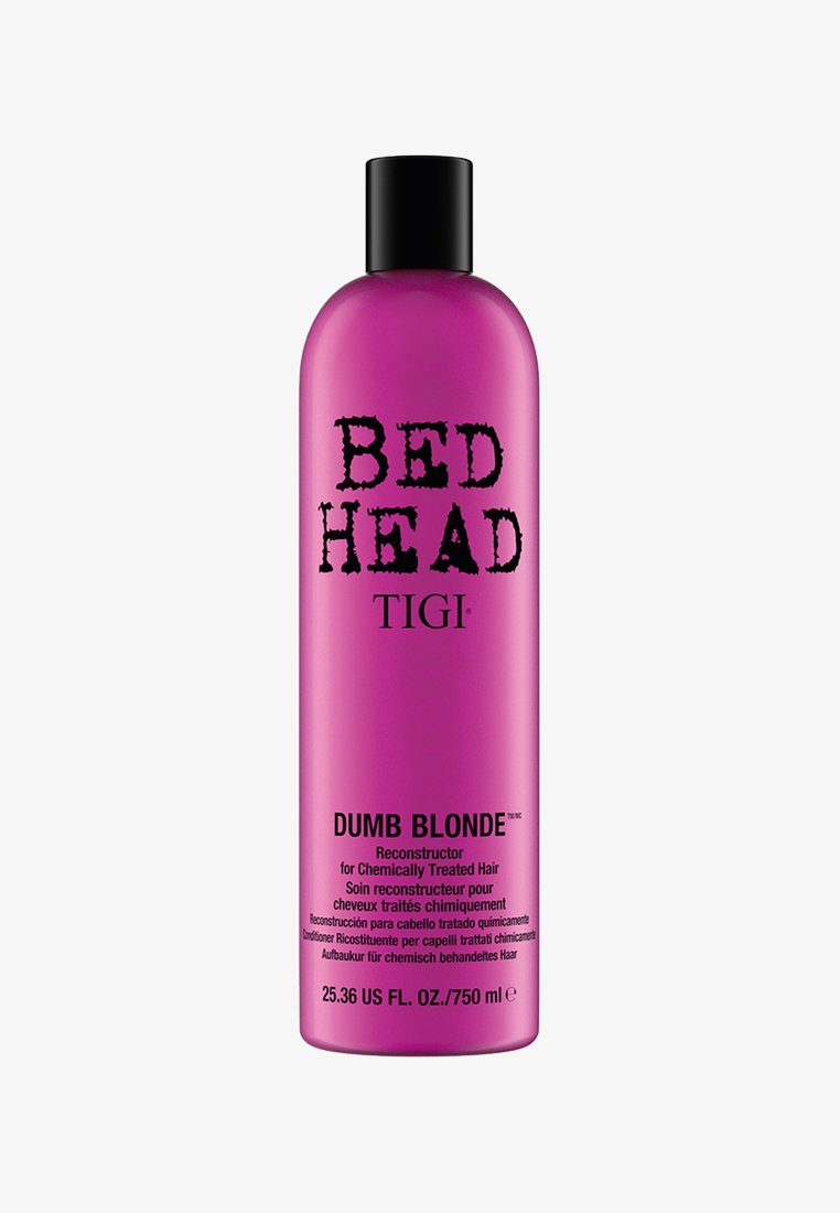 Vaaleanpunainen muovipullo, jossa on musta korkki, etiketti "BED HEAD TIGI DUMB BLONDE." Tekstissä on tuotedetaljeja englanniksi ja useilla muilla kielillä.
