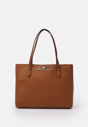 Sac fourre-tout en cuir marron avec doubles poignées et logo métallique "GUESS" sur le devant, sur fond blanc.