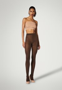 Brune fiskenetstrømper med et tekstureret mønster parret med en tætsiddende beige cropped top. Model iført nude høje hæle.