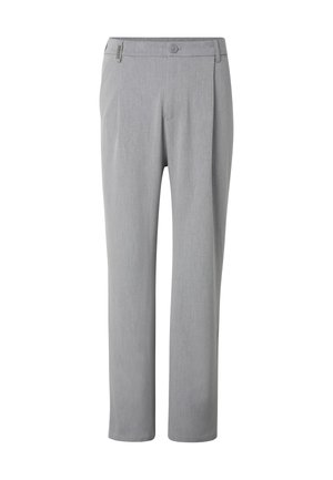 Personne portant un pantalon gris clair, des baskets blanches et une veste zippée marron avec une chemise blanche en dessous.