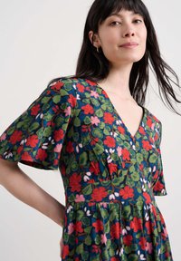 Robe fleurie à manches courtes, avec un fond bleu orné de fleurs rouges, roses et vertes ; décolleté en V et tissu texturé.