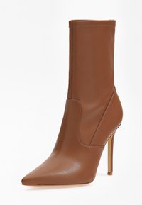 Botte de cheville à talon aigu en cuir marron avec un bout pointu, un talon slim et des coutures visibles sur le bord supérieur et les panneaux latéraux.