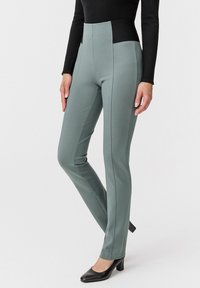 Pantaloni verdi a vita alta con un design aderente. Realizzati in tessuto liscio, presentano dettagli delle cuciture e una cintura nera a contrasto.