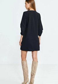 Czarna sukienka z rękawami do łokcia, dopasowany fason i suwak z tyłu. Noszona z beżowymi kozakami zamszowymi sięgającymi do kolan. Gładka tekstura.