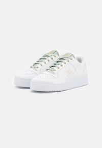 Sneakers bianchi con una finitura testurizzata, lacci verdi, occhielli dorati e un logo. Presentano una spessa suola in gomma bianca e una punta perforata.