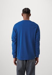 T-shirt bleu à manches longues en tissu doux, avec un col rond et une coupe décontractée, associé à un pantalon en denim gris.