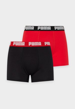 Un mannequin masculin se tient devant un fond blanc, portant un boxer Puma noir à ceinture orange.