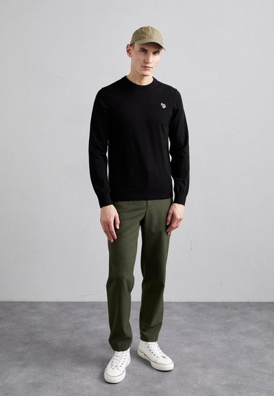 Μαύρη πουλόβερ, μονής υφής, με μακριά μανίκια, σε συνδυασμό με ελαιόλαδα παντελόνια και λευκά αθλητικά παπούτσια. Περιλαμβάνει ένα ανοιχτό πράσινο καπέλο.