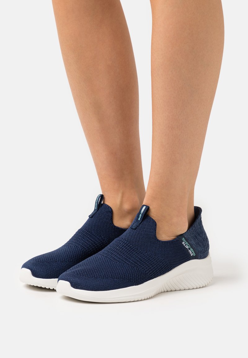 Marine slip-on schoenen met een textuur gebreide bovenkant, witte rubberen zool en donkerblauwe hielaccenten. Voorzien van aantrektabs voor gemakkelijk aan- en uittrekken.