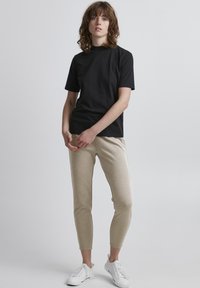 Czarny krótki rękaw T-shirt w połączeniu z beżowymi dopasowanymi joggerami. Joggerzy mają gładką teksturę, a model nosi białe trampki.