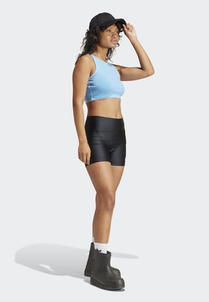Športový modrý crop top, čierne šortky s vysokým pásom a masívne čierne čižmy. Model má na sebe čierny klobúk a biele vysoké ponožky s logom.