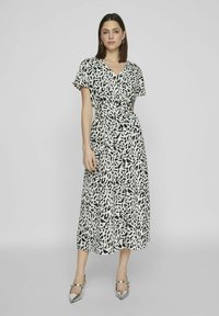 Czarna i biała sukienka w wzory z krótkimi rękawami, dekoltem w serek, paskiem w talii oraz zwiewną spódnicą. Modelka zestawiła ją z metalicznymi szpilkami.