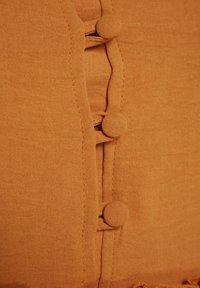 Gros plan d’un tissu orange avec trois boutons recouverts fixés à travers des boucles en tissu le long d’une couture.
