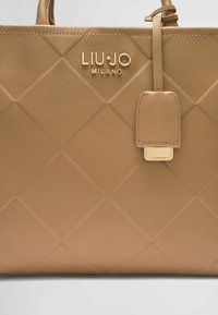 Borsa a tracolla in pelle color cuoio con motivo a rombi trapuntati, logo dorato e etichetta attaccata. Le caratteristiche includono manici doppi e texture liscia.
