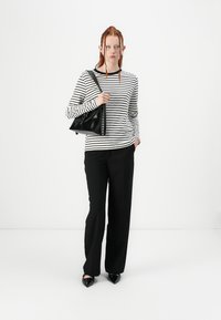 Camisa de rayas en blanco y negro de manga larga combinada con pantalones anchos negros y zapatos negros de punta, con un bolso negro texturizado.